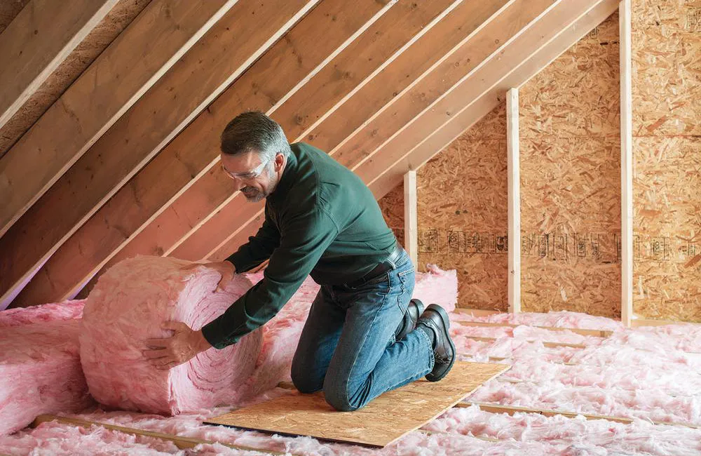 Contractor installing fiberglass batt insulation in an attic